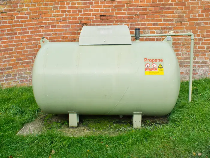 A large propane tank against a red brick wall